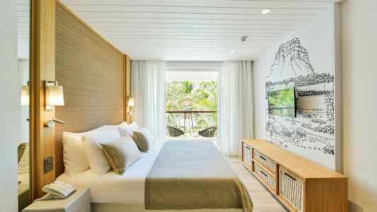 Ett hotellrum med en säng, en TV och en balkong med utsikt mot ett palmträdsområde. (AI-genererad text)