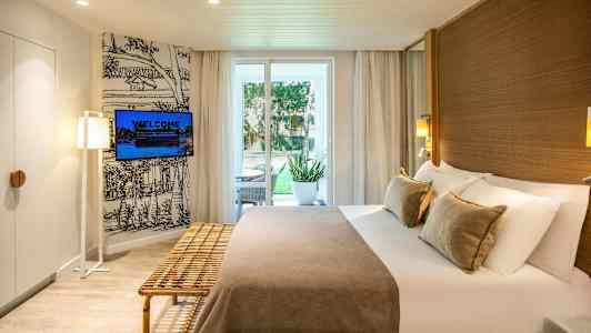 Hotellrum med dubbelsäng, sittmöbler utomhus vid dörren och vägg-tv. (AI-genererad text)