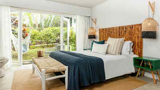 Ett sovrum med dubbelsäng, trädetaljer och stora fönster mot en grön utsikt. (AI-genererad text)