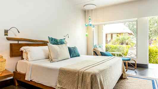 Ett ljust sovrum med en dubbelsäng och stora fönster ut mot en grönskande trädgård. (AI-genererad text)