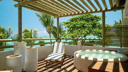 Ett trädeck med en solstol, tre vita blomkrukor och en bubbelpool, med utsikt över havet och omgivande palmer. (AI-genererad text)