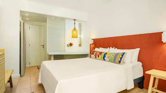 Hotellrum med en dubbelsäng, färgglad kudde och en orange sänggavel. (AI-genererad text)