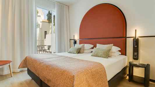 Modern hotellrum med dubbelsäng, röd huvudgavel och stora fönster mot en balkong. (AI-genererad text)