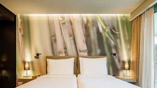 Två enkelsängar med vita lakan framför en vägg med bambumotiv. (AI-genererad text)