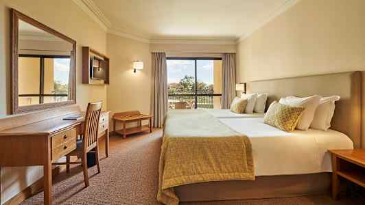 Bild av ett hotellrum med en dubbelsäng, arbetsbord och stolar samt en balkong med utsikt. (AI-genererad text)