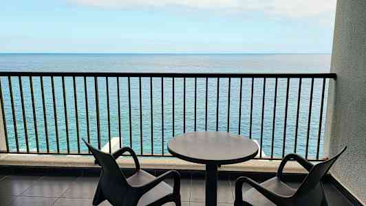 Två stolar och ett bord på en balkong med havsutsikt. (AI-genererad text)