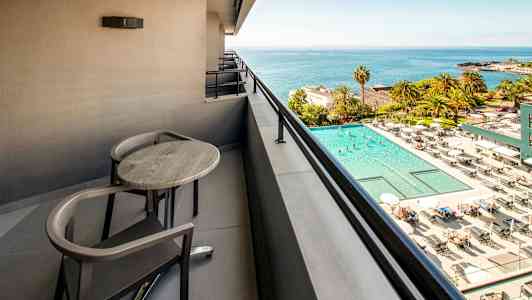 Balkong med bord och stolar med utsikt över en pool och havet. (AI-genererad text)