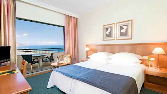 Hotellrum med dubbelsäng, nattduksbord och balkong med utsikt över havet. (AI-genererad text)