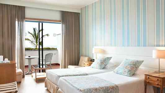 Ett hotellrum med två enkelsängar, dekorativa kuddar och en balkong utrustad med stolar och bord. (AI-genererad text)