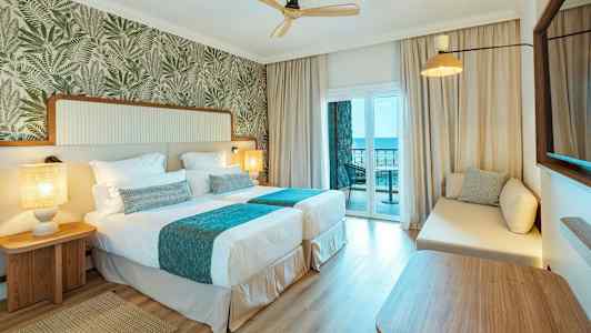 Hotellrum med två enkelsängar och en balkong med havsutsikt. (AI-genererad text)