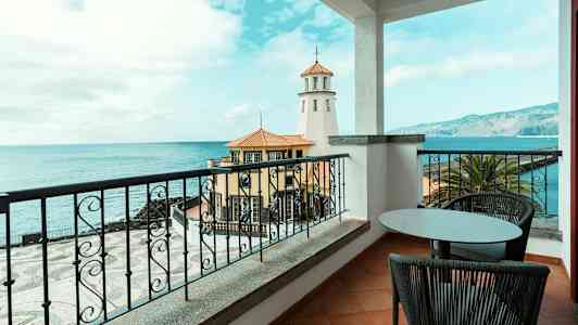 Utsikt från en balkong mot havet, med en fyr och byggnader i förgrunden. (AI-genererad text)
