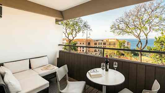 En terrass med sittgrupp och utsikt mot havet, med bord och två glas vin. (AI-genererad text)