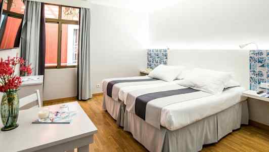 Hotellrum med två sängar, ett bord med dekorativ vas och ett fönster. (AI-genererad text)