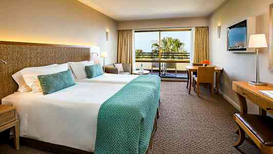 Ett hotellrum med två enkelsängar, en sittgrupp, ett skrivbord och en balkong med utsikt. (AI-genererad text)