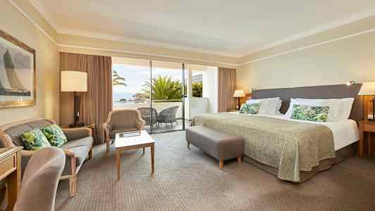 Ett hotellrum med stor säng, sittgrupp och en balkong med utsikt. (AI-genererad text)