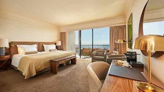 Ett stilfullt hotellrum med en dubbelsäng, skrivbord och sittgrupp, samt stora fönster mot en balkong. (AI-genererad text)