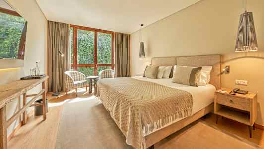 Ett hotellrum med en bred säng, två fåtöljer vid ett fönster och ett bord. (AI-genererad text)