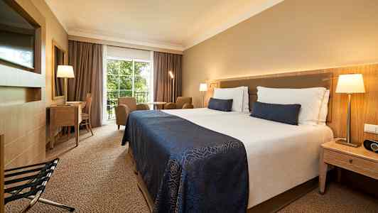 Hotellrum med dubbelsäng, sittområde, skrivbord och utsikt mot grönska. (AI-genererad text)