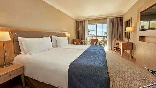 Hotellrum med två enkelsängar och en balkong med utsikt. (AI-genererad text)