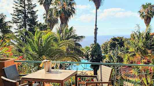 Matbord på en terras med utsikt över tropiska träd, en pool och havet. (AI-genererad text)