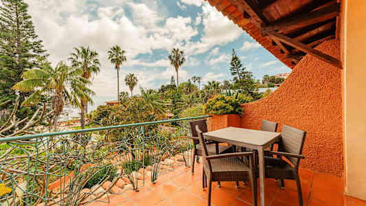 En terrass med bord och stolar omgiven av grönska och palmer. (AI-genererad text)