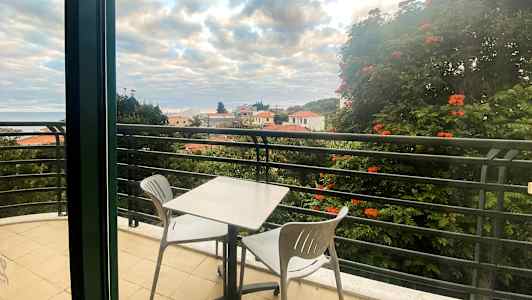 En balkong med ett bord och två stolar, utsikt över hustak och träd. (AI-genererad text)