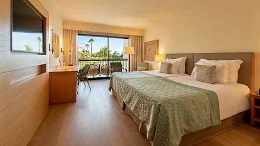 Modernt hotellrum med dubbelsäng och balkong i bakgrunden. (AI-genererad text)