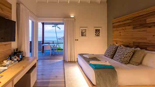 Ett hotellrum med en stor säng och utgång till en terrass med utsikt över havet. (AI-genererad text)