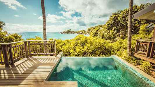 Utsikt från en träterrass och en pool över en tropisk trädgård och havet. (AI-genererad text)