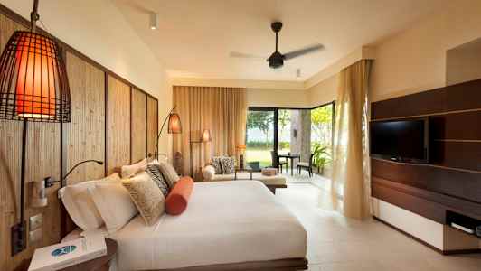 Ett hotellrum med en stor säng, soffgrupp och en tv, samt utsikt mot en grönskande trädgård. (AI-genererad text)