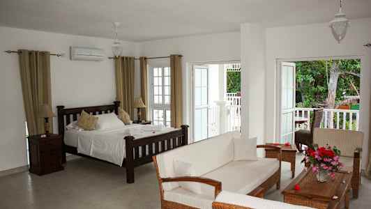 Ett ljust hotellrum med en säng, soffa och öppna dörrar till en balkong med naturutsikt. (AI-genererad text)