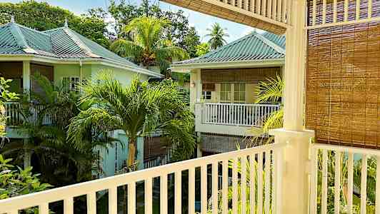 En vy från en balkong som visar ett grönskande område med pastellfärgade hus och palmträd. (AI-genererad text)