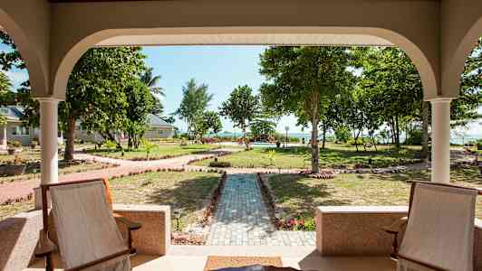 Utsikt från en veranda mot en välskött trädgård med gångvägar och träd. (AI-genererad text)