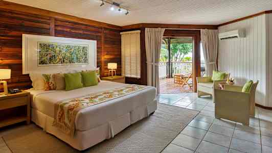 Ett hotellrum i varma toner med en säng, sittmöbler och en terrass med utsikt över grönska. (AI-genererad text)