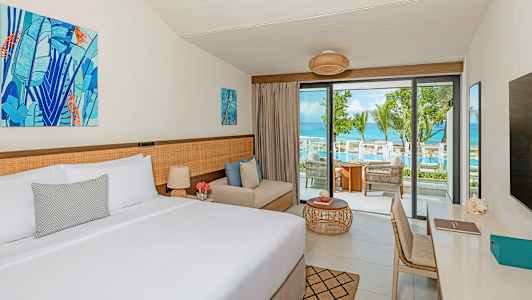 Ett hotellrum med en dubbelsäng, en sittplats och en balkong med utsikt över en pool och havet. (AI-genererad text)