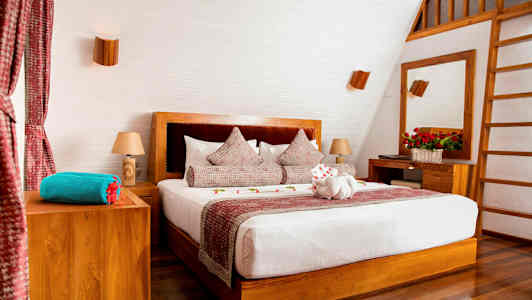 Ett stilrent sovrum med en dubbelsäng, trädetaljer och dekorerade kuddar. (AI-genererad text)