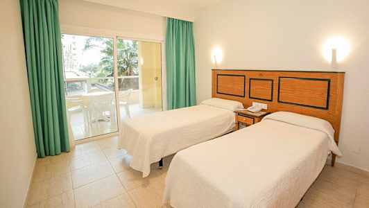 Hotellrum med två enkelsängar, en liten uteplats med möbler och palmträdsutsikt. (AI-genererad text)