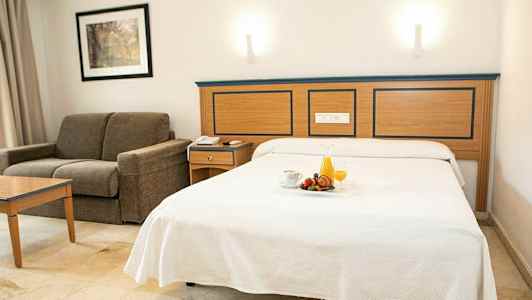 Hotellrum med bäddad säng och soffa. (AI-genererad text)