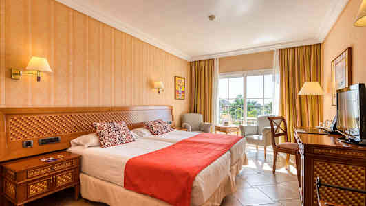 Bild på ett hotellrum med två sängar, stol och bord, samt en TV. (AI-genererad text)