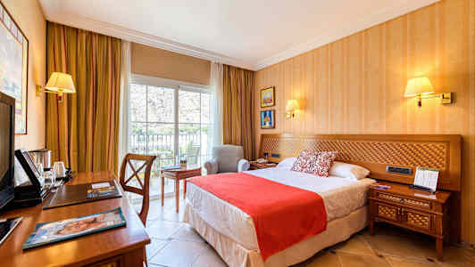 Ett hotellrum med en säng, sängbord, skrivbord och en fåtölj vid ett fönster. (AI-genererad text)