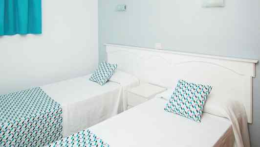 Två enkelsängar med vit sängklädsel och mönstrade kuddar och överkast. (AI-genererad text)