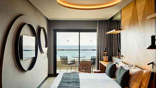 Ett modernt hotellrum med säng, speglar på väggen, skrivbord och en balkong med utsikt över havet. (AI-genererad text)