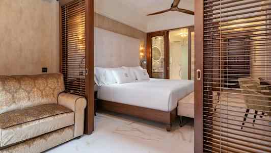 Ett hotellrum med en dubbelsäng och en soffa, avskärmat med träpersienner. (AI-genererad text)