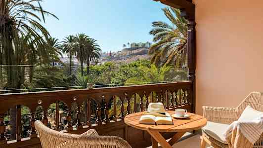 Terrass med bord, bok och solhatt, utsikt över palmer och byggnader. (AI-genererad text)