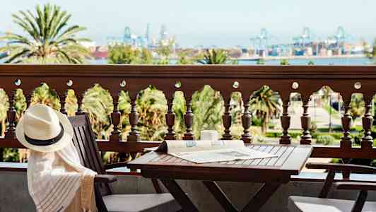 En balkong med bord och stolar, utsikt över träd och industriområde i fjärran. (AI-genererad text)