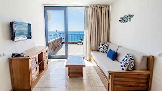 Ett hotellrum med sittgrupp och utsikt mot havet från en balkong. (AI-genererad text)