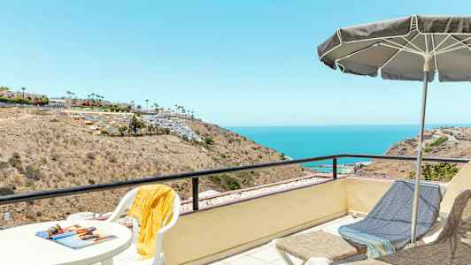 En utsiktsplats med bord och stolar, en parasoll samt solstolar som blickar ut över ett kustlandskap och havet. (AI-genererad text)