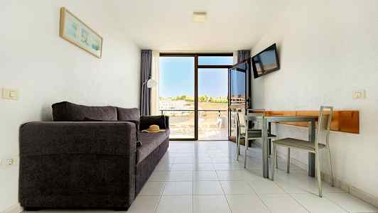 Ett vardagsrum med en mörk soffa, ett matbord med stolar och en balkong med utsikt. (AI-genererad text)