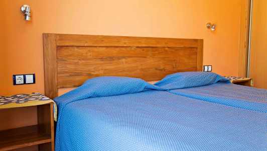 En säng med blå prickiga sängkläder och en trä huvudgavel mot en orange vägg. (AI-genererad text)