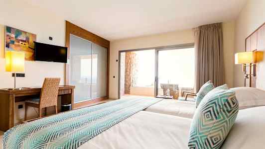 Bild av ett hotellrum med två sängar, en skrivbordsplats, en TV och en balkong med stolar. (AI-genererad text)